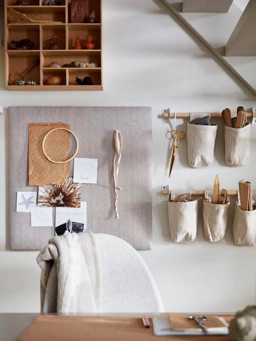 Living space with textile containers hung on rails placed on the wall, a desk, a chair, personal belongings, a shelving unit.