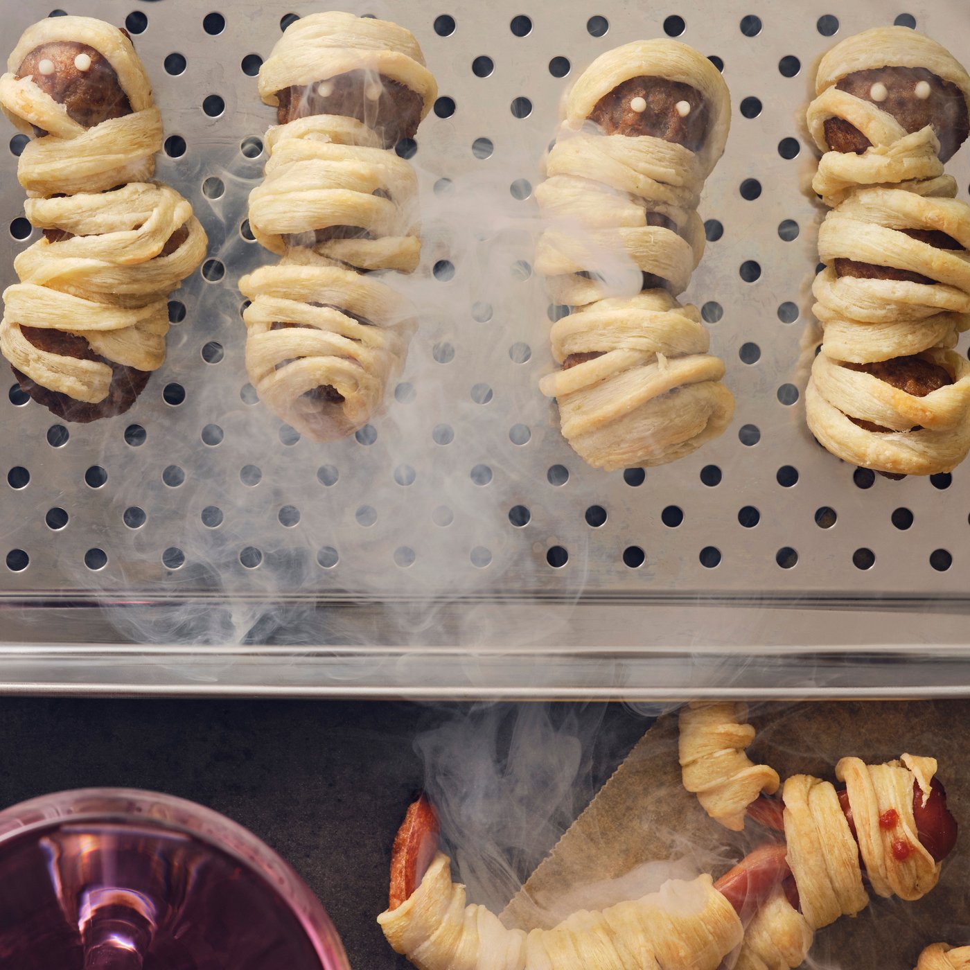Four meatball mummies with HUVUDROLL plant balls or meatballs and puffed pastry strips on a stainless steel dish with smoke.