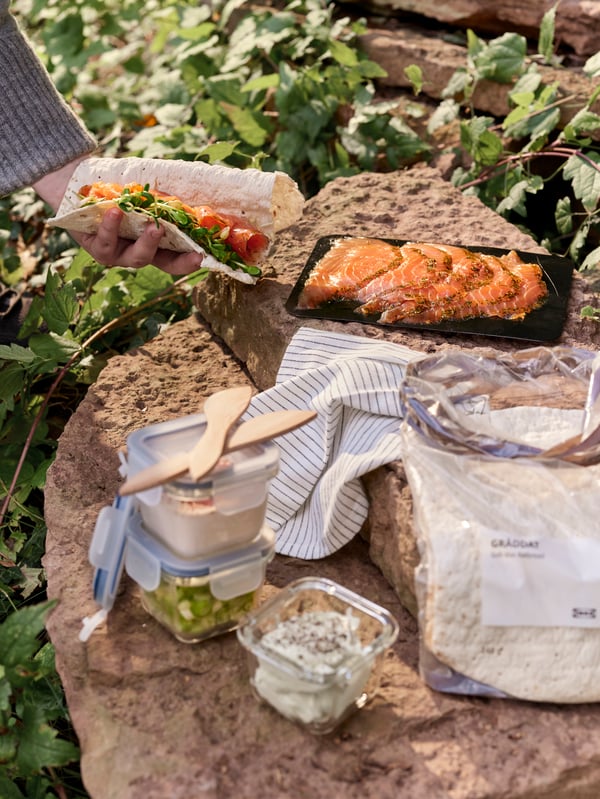 A sunlit stone slab with SJÖRAPPORT cured salmon, GRÄDDAT soft thin flatbread and side dishes in IKEA 365+ food containers.