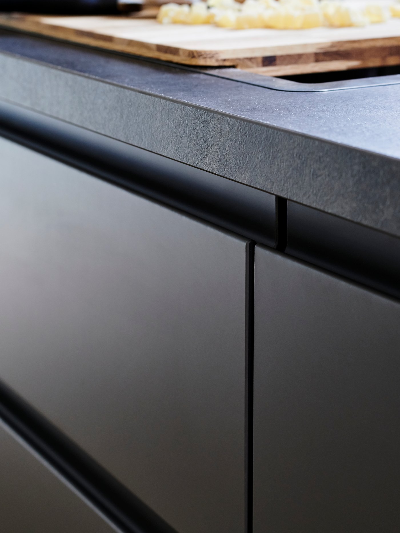 Detalle de una cubierta de cocina laminada color grafito, sobre un mueble del mismo color con cajones lisos sin tirador.