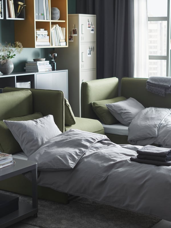 A living room with two green VALLENTUNA sofa-beds that are made as beds.