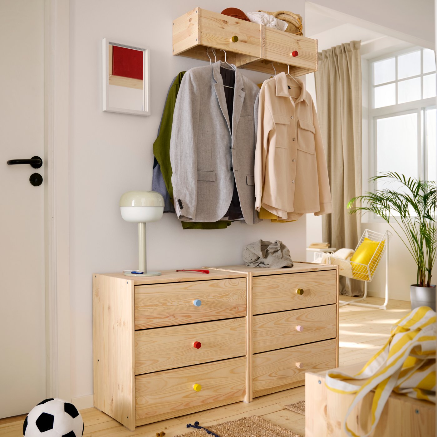 A beige BLÅSVERK table lamp is on one of two side-by-side RAST chests of 3 drawers in an entryway. A coatrack is above them.
