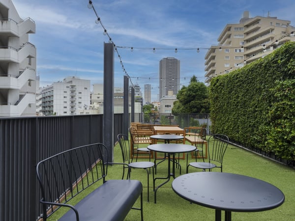 金属製ベンチと丸テーブルが並ぶ屋上。ストリングライトと緑が彩る都市型アウトドア空間