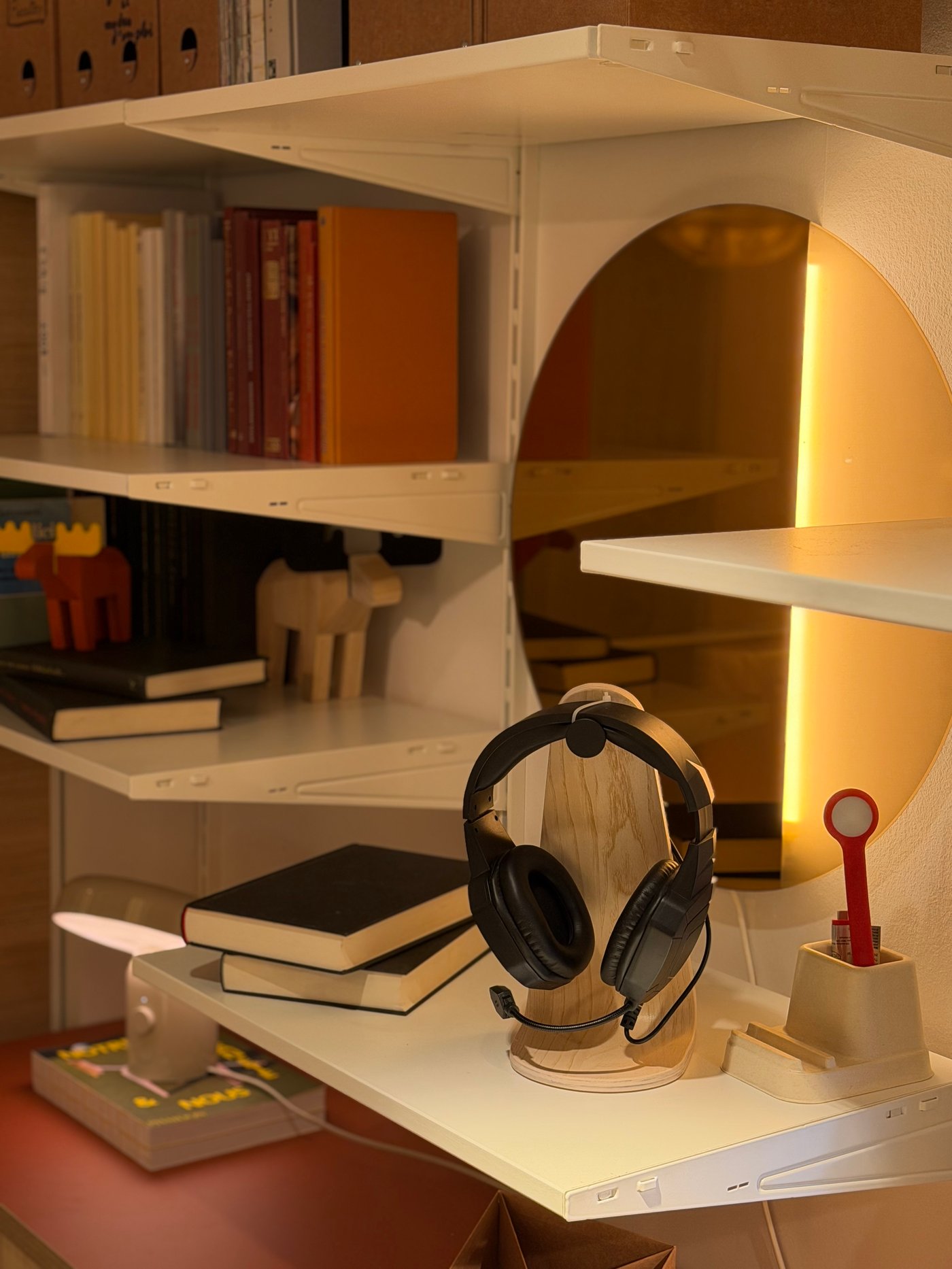 La vue d'un coin du salon avec un miroir rond, un casque audio, et des livres sur des étagères blanches