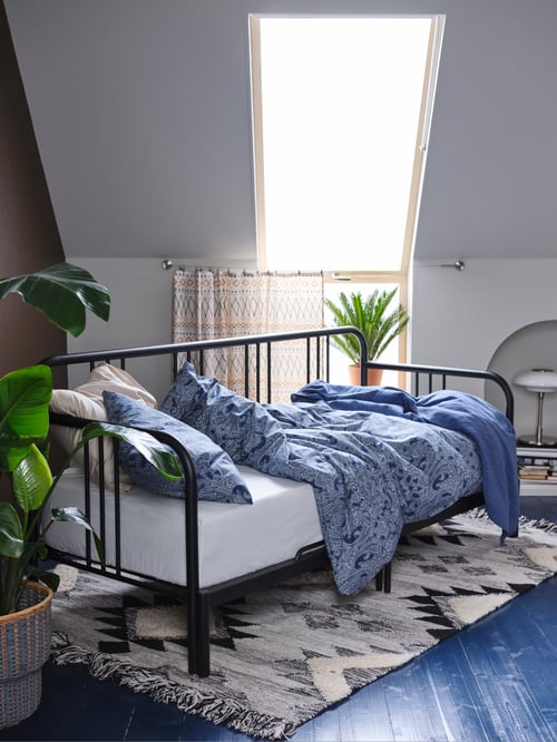 Bedroom with a black day bed frame made of steel, placed on a rug flatwoven and covered by a duvet cover with pillowcase.