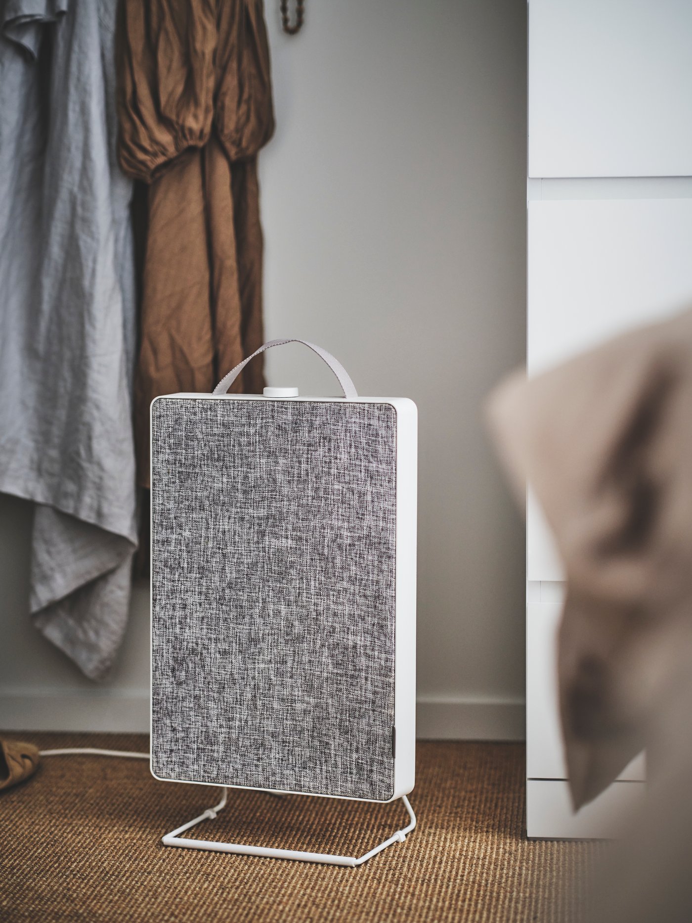 A light grey FÖRNUFTIG air purifier placed on the bedroom floor next to a white chest of drawers.