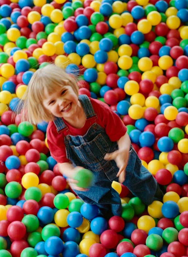 A little girl smiling in a ball pool full of colourful balls. 