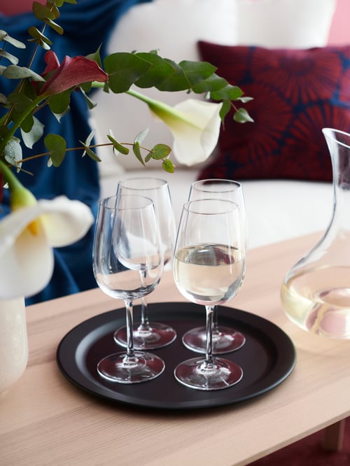 Four STORSINT white wine glasses on a round black serving platter with flowers in the foreground.
