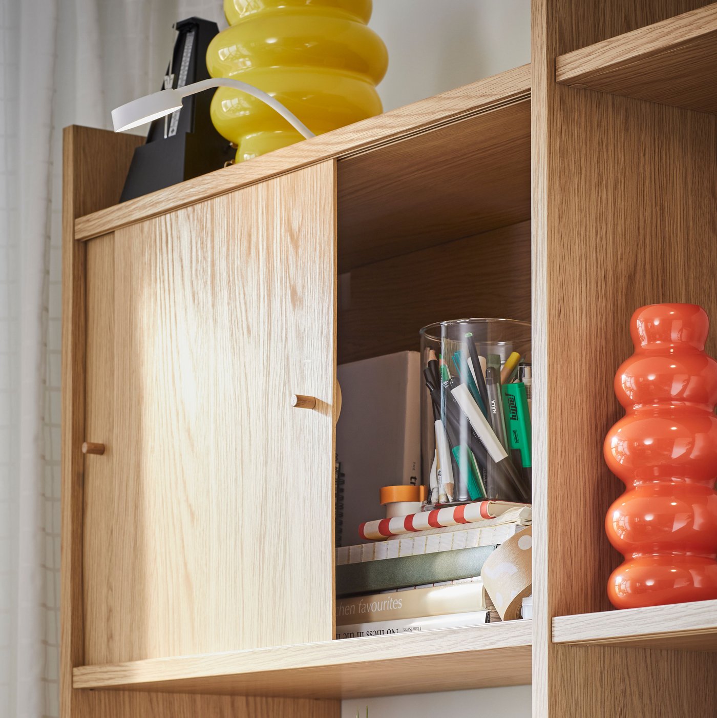 Del av förvaringskombination LÅDMAKARE med två skjutdörrar öppna och med en orange KÄLLARHALS-vas på ett hyllplan.