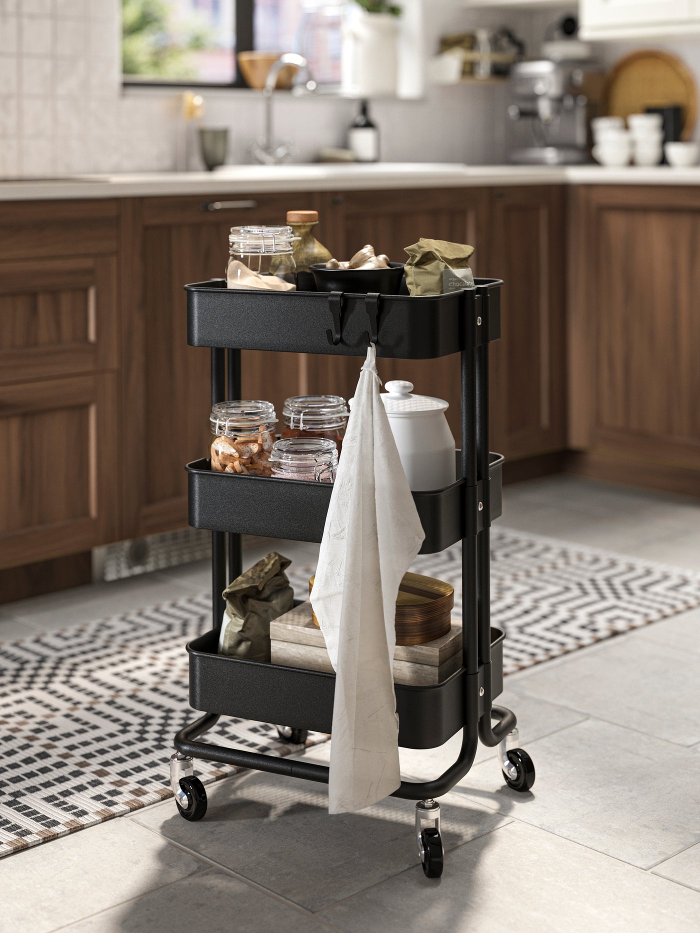 Un carrito de cocina RÅSKOG negro con especieros y frascos de vidrio en sus bandejas.
