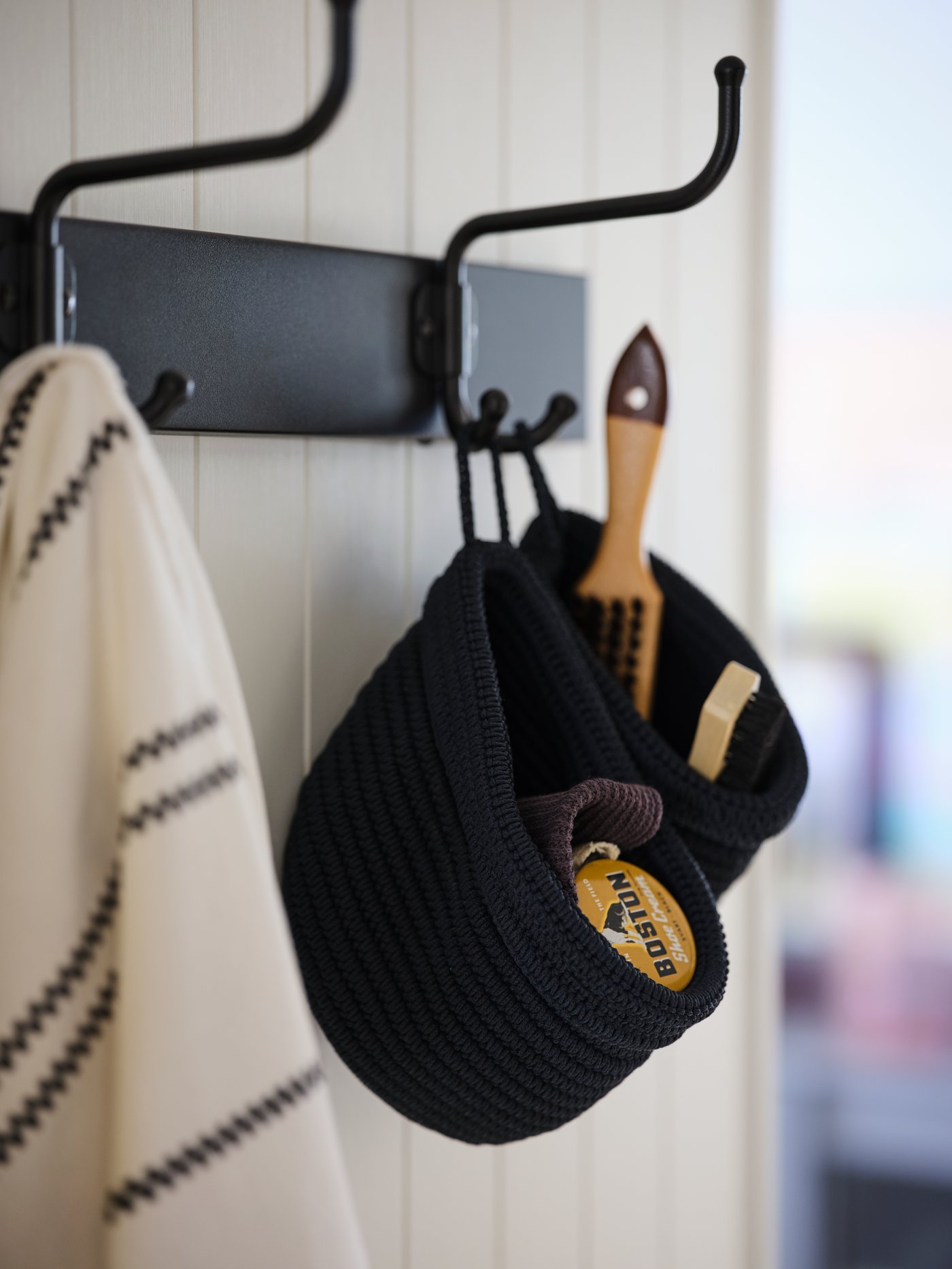 Deux paniers NORDRANA bleus contenant des accessoires de soin des chaussures accrochés à une patère avec 3 crochets PINNIG sur un mur en bois blanc.