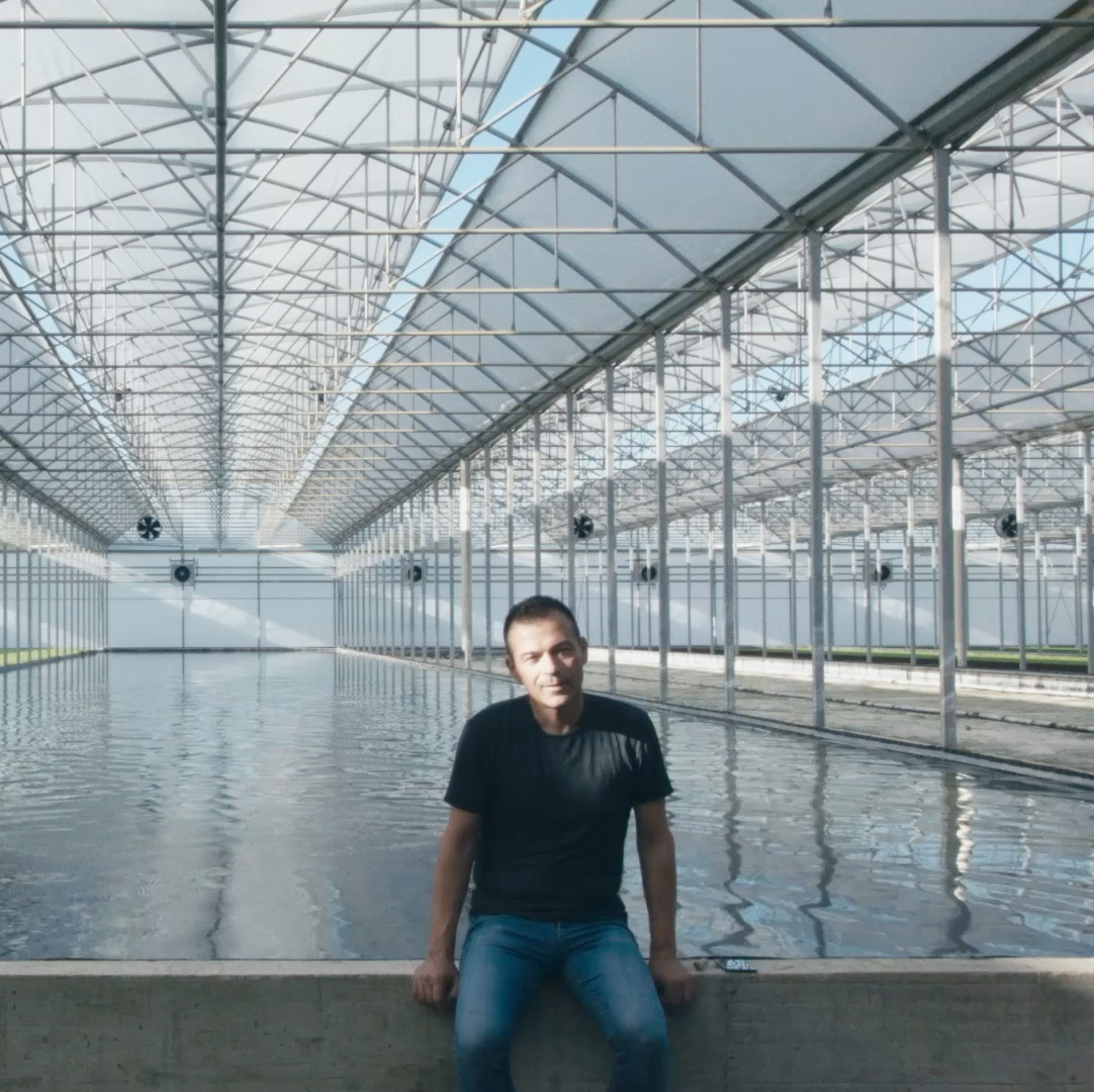 Čovek sedi na ivici bazena u staklenoj zgradi.