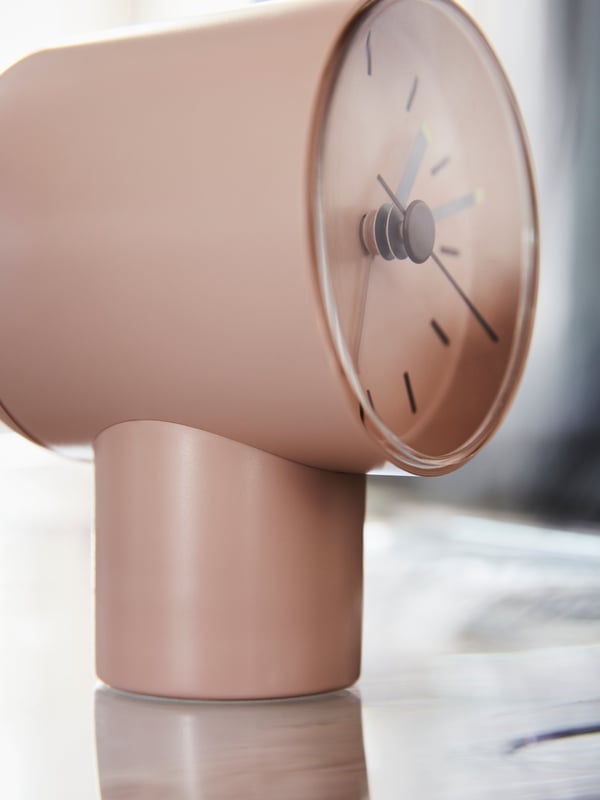 A light, dimly sunlit surface on which stands a pale-pink BONDTOLVAN analog alarm clock.