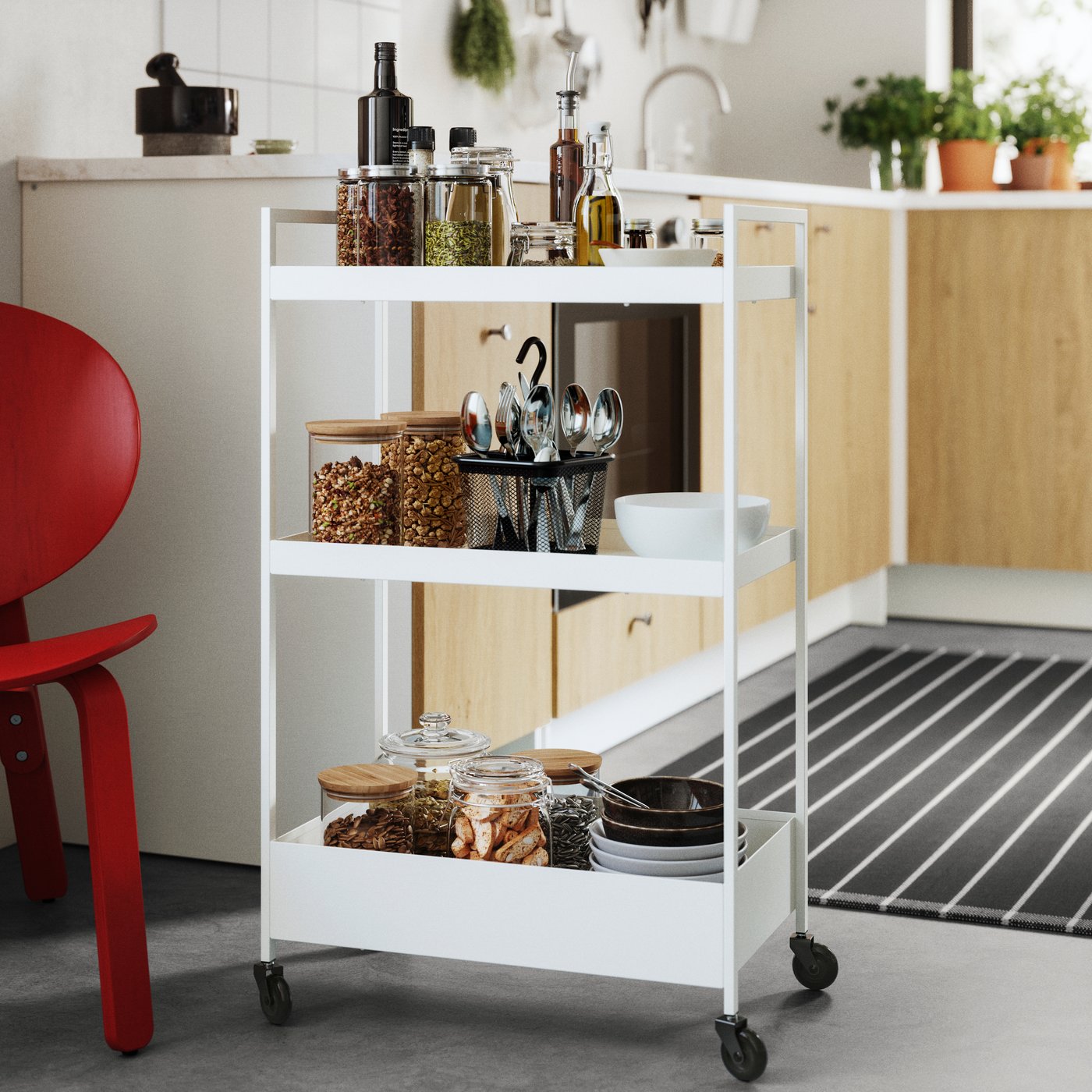 A white NISSAFORS trolley with jars, utensils, and oils in a bright kitchen setting with wooden cabinets.