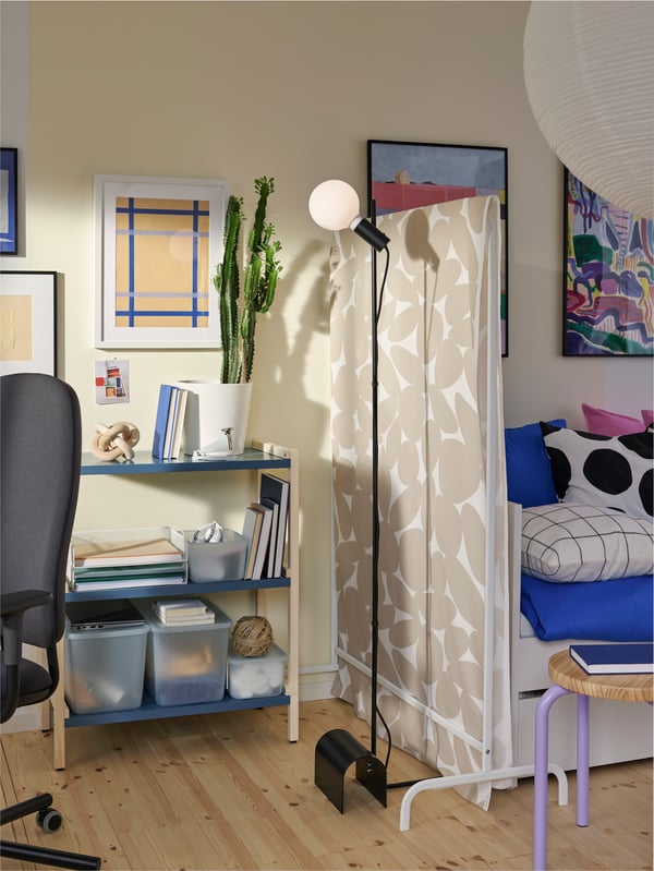 An EKENABBEN open shelving unit with storage accessories next to a floor lamp and a clothes rack with a draped fabric.