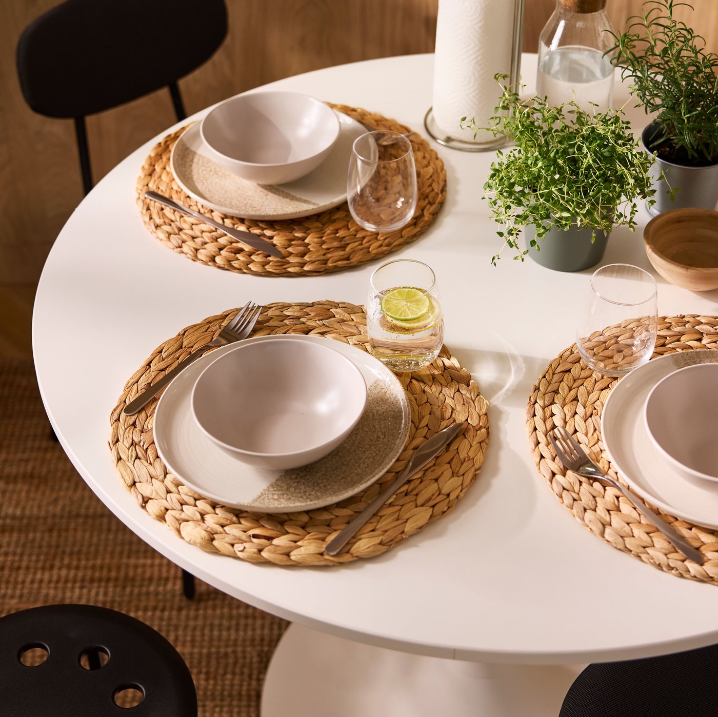 A sun-dappled dining area with a white, round DOCKSTA table set with potted herbs and tableware on round SOARÉ place mats.