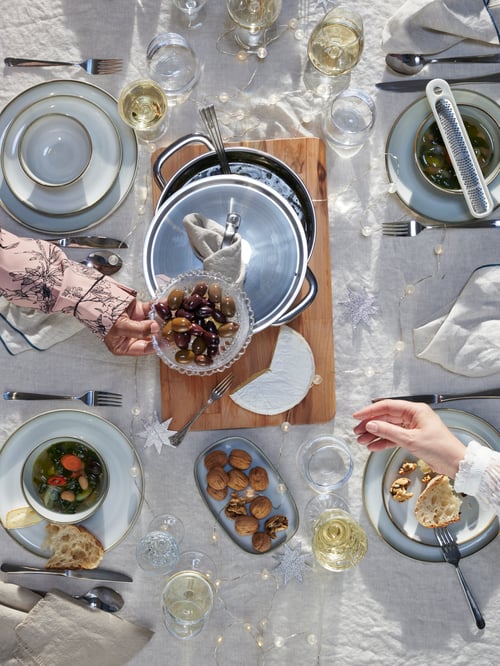 Blick von oben auf einen gedeckten Esstisch mit einem IKEA 364+ Topf mit Deckel in der Mitte, aus dem Suppe in GLADELIG Schüsseln verteilt werden. Außerdem sind auf dem Tisch GLADELIG Teller und Dessertteller zu sehen sowie gefüllte SÄLLSKAPLIG Weingläser.