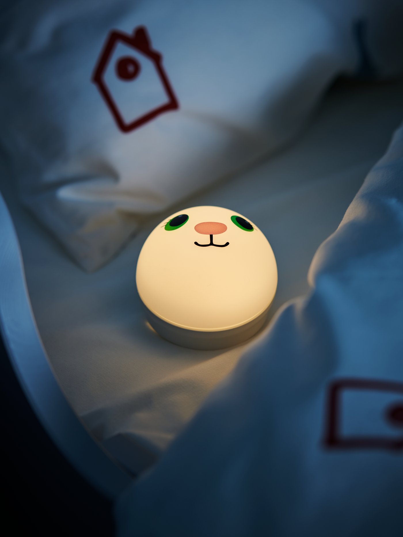 Una lámpara infantil redonda con una carita de animal dibujada. La lámpara está encendida dentro de una cuna.