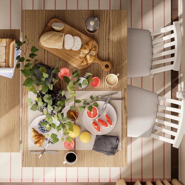 An eagle-eye’s view of an ÅLHULT table with a bench and chairs. The table is set for a brunch with bread, coffee and fruit.
