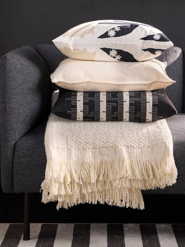 En stabel med hvit og svart mønstrert puter på en svart sofa.