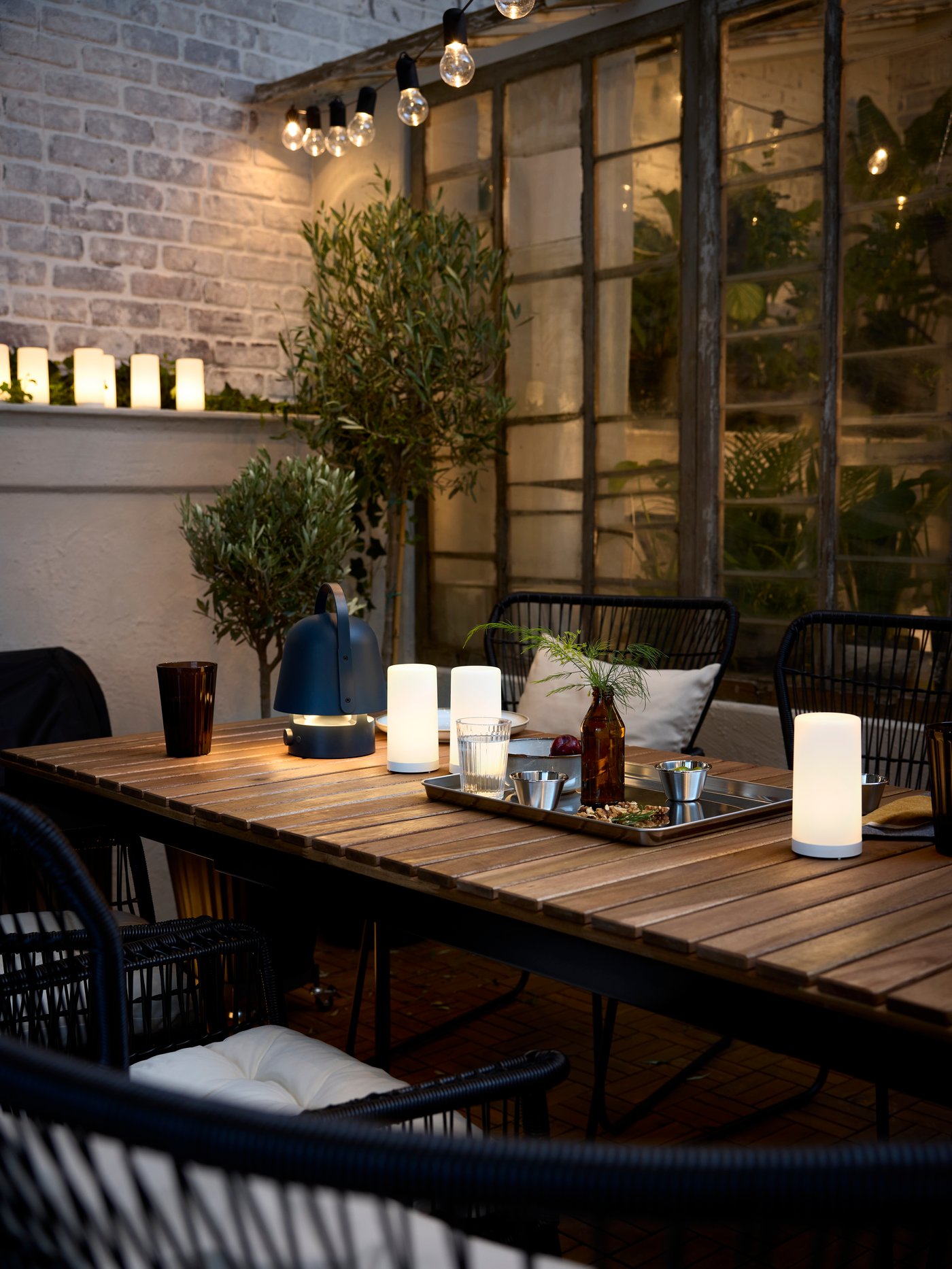 A VÄSMAN extendable outdoor table with SOLVINDEN LED decoration lighting and a blue VAPPEBY bluetooth speaker lamp on it.
