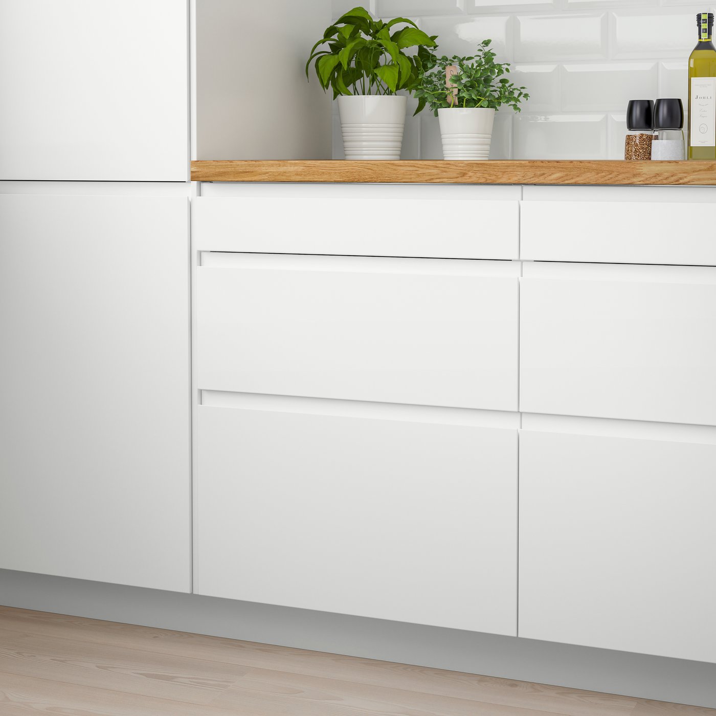 Hvide køkkenskabe med matte låger og integrerede greb. På bordpladen står to grønne potteplanter. 