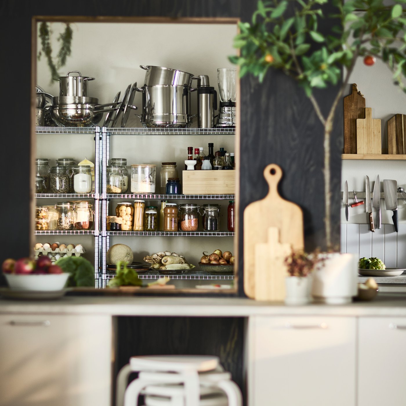 Een warme en overzichtelijke IKEA-keuken toont metalen rekken vol voorraadpotten, kruiden, etenswaren en roestvrijstalen keukengerei, terwijl snijplanken, messen en planten voor een natuurlijke uitstraling zorgen.