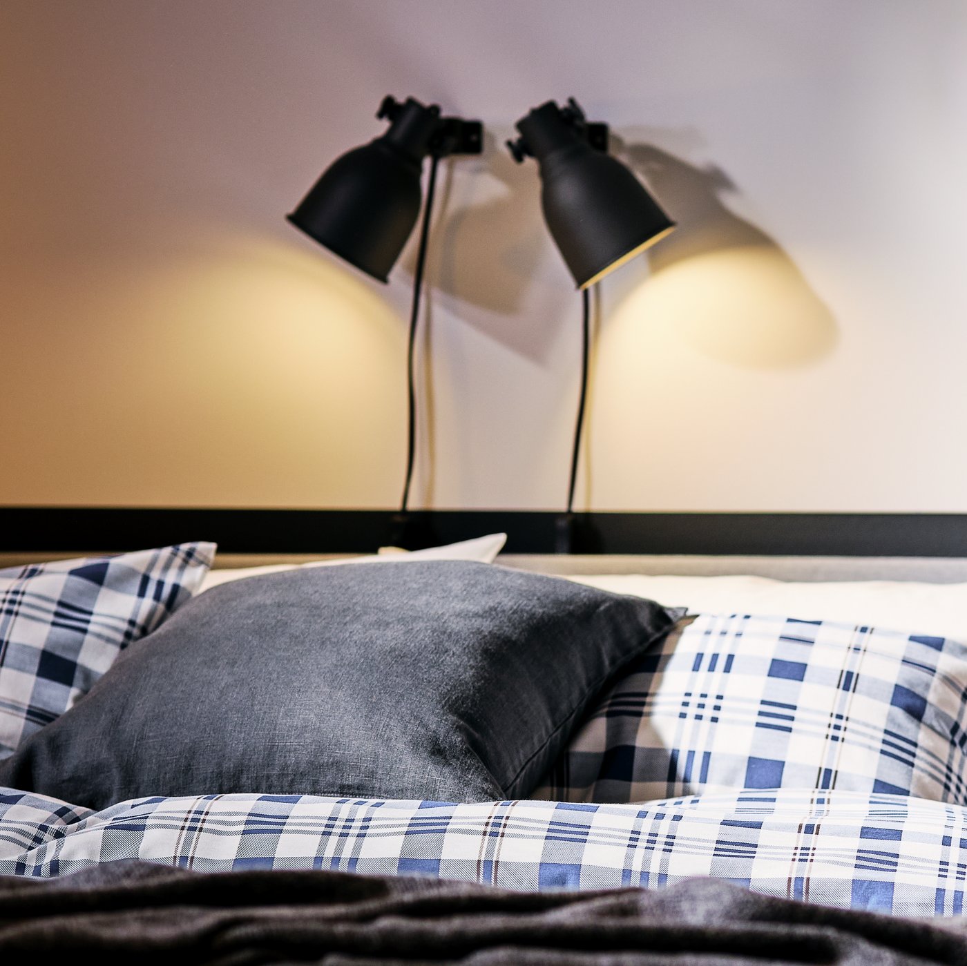 The head end of a light-grey SLATTUM bed made with SPIKVALLMO bed linen, lit up by double, dark-grey HEKTAR spotlights.