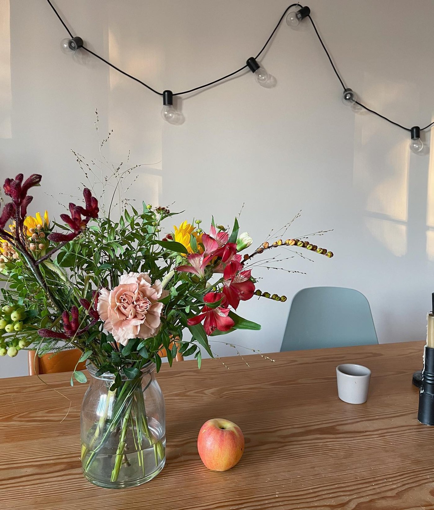 Comedor con una guirnalda luminosa LED BLÖTSNÖ de 24 luces colocada detrás de una mesa con un jarrón BEGÄRLIG.