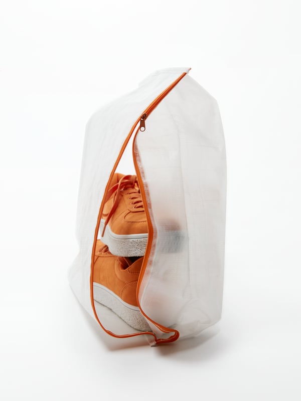 A PÄRKLA shoe bag in a white studio space. The zip of the storage bag is open to reveal a pair of orange casual shoes.