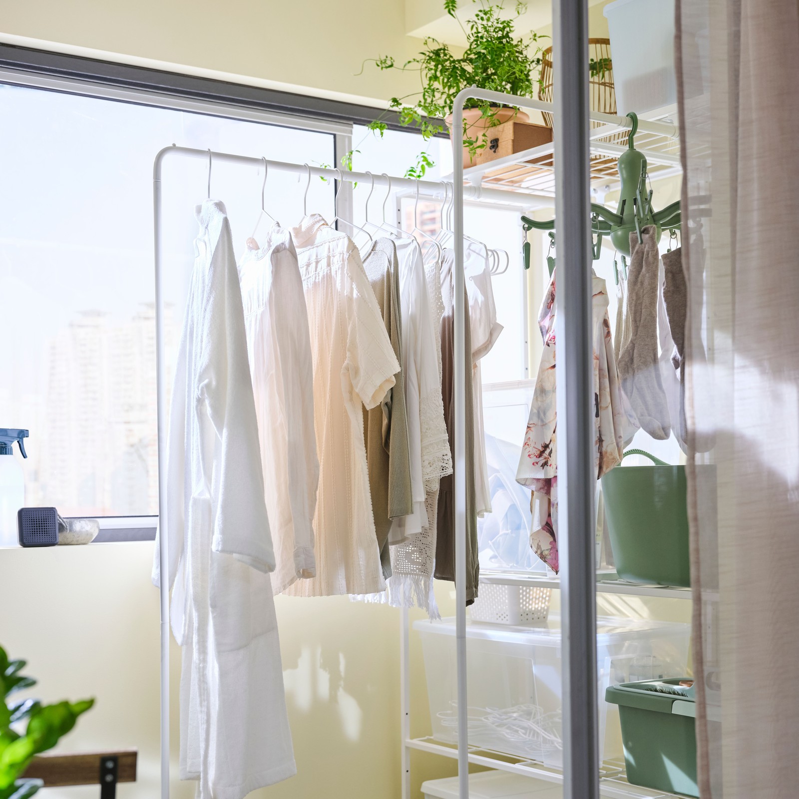 Two white JOSTEIN shelving units with drying racks are side by side on an enclosed balcony wall, with clothes on the racks.