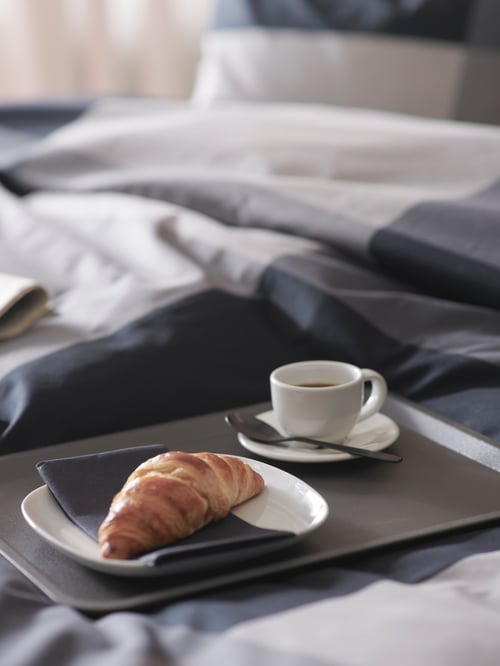 Close-up shot of TILLGÅNG tray in bed, VÄRDERA side plate with croissant, VARDAGEN espresso cup, saucer, and spoon.