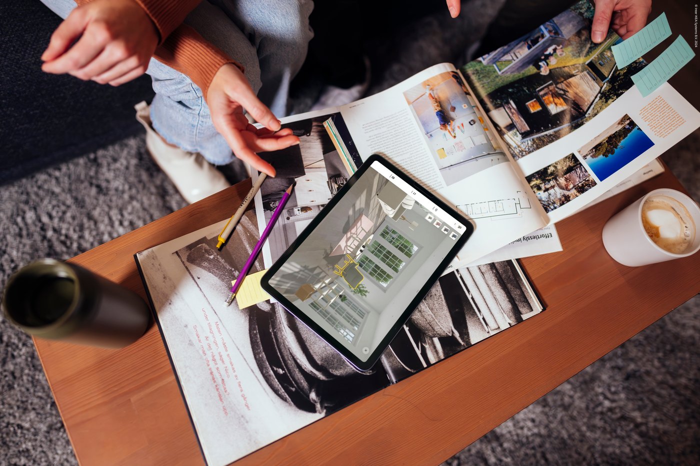 A person has the IKEA Kreativ app open on their phone. In the background, a mood board lies on a coffee table.
