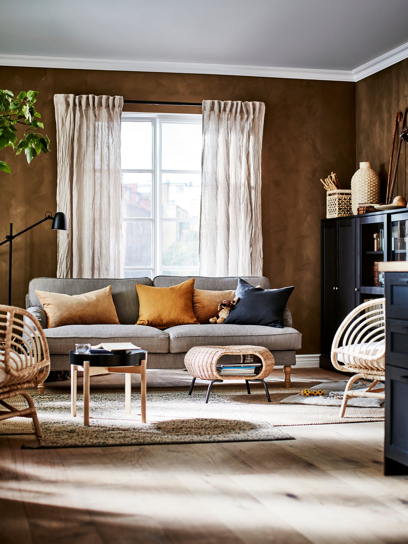 A living room with a sofa, two jute rugs, two rattan armchairs, beige linen curtains and cabinets.