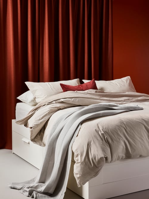 Bedroom with red walls, room darkening shades, white bedframe with drawers, quilt cover and pillowcases, cushion covers. 