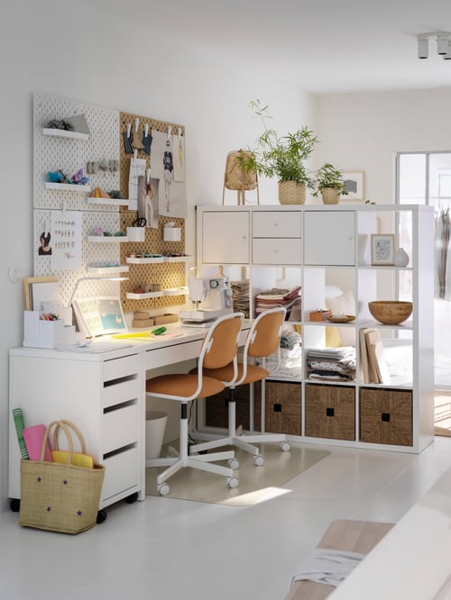 Bureau MICKE blanc entre un caisson-tiroirs et un meuble séparateur de pièce assortis. Deux chaises sont placées sous le bureau.