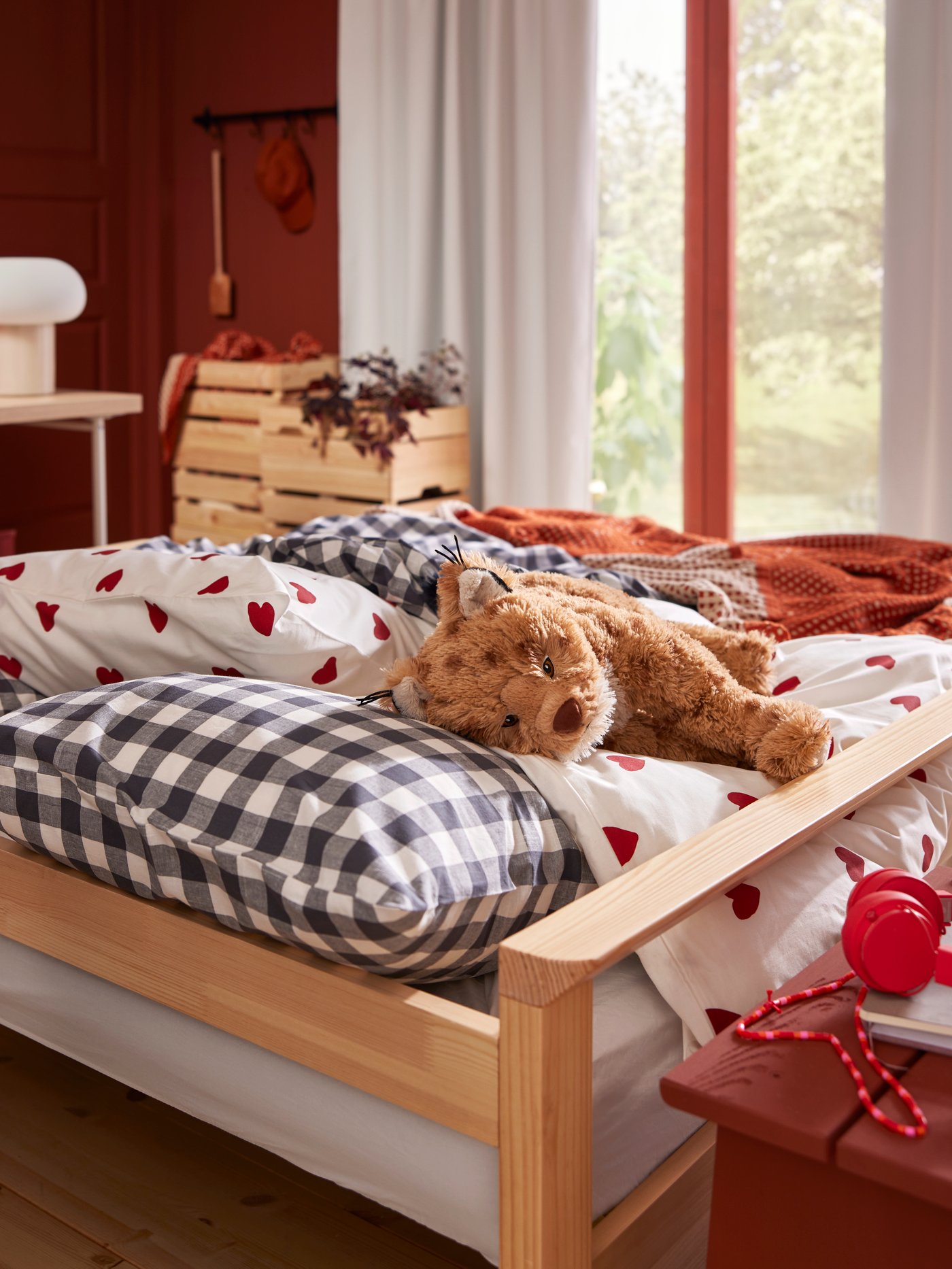 A SKOGSDUVA soft toy lynx lies on a sofa-bed with white and red BARNDRÖM bed linen and checked EKTANDVINGE bed linen.