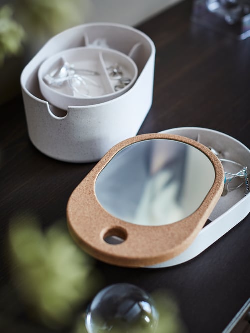 Un prim-plan modern al dormitorului cu o cutie ovală de depozitare cu capac de oglindă, realizată din plută și material plastic compozit din lemn.