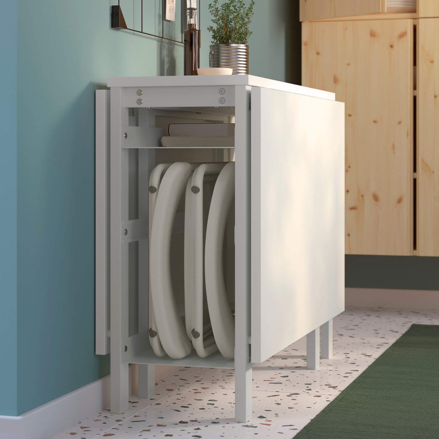A white VIHALS gateleg table with the surface folded, and with folding chairs tucked inside the storage compartment.