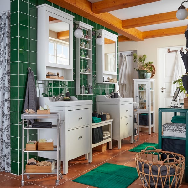 A bathroom with green tiles, two white HEMNES wash-basins and mirror cabinets, towels and accessories on display.