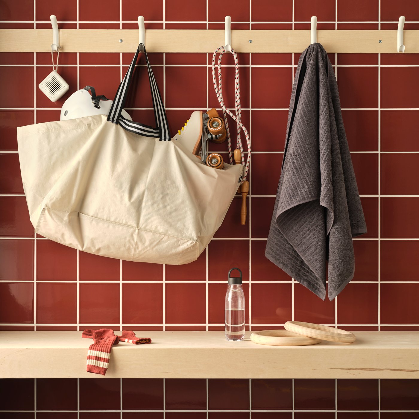 A tiled wall with a GÖRSNYGG carrier bag and VÅGSJÖN towel hanging on hooks, an IKEA 365+ water bottle on a bench.
