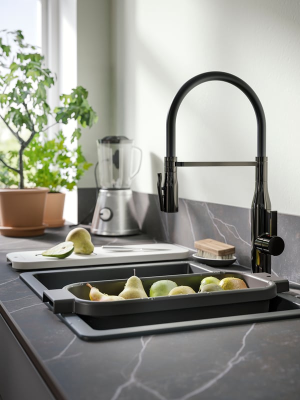 A black KILSVIKEN inset sink bowl has a colander filled with fruit and a TOLLSJÖN kitchen mixer tap in black polished metal.