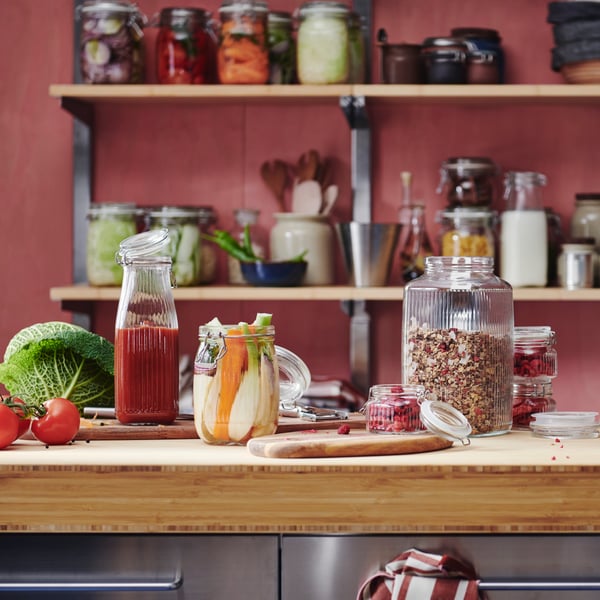A KÖSSEBÄR jar with lid sits beside other jars in different shapes, all filled with food and drinks, on a bamboo worktop.