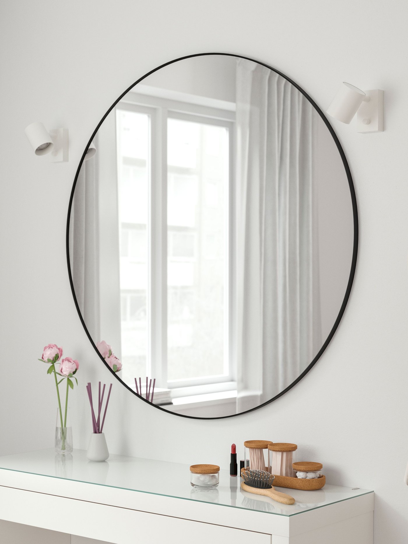 Un grand miroir rond noir au-dessus d’une coiffeuse blanche.