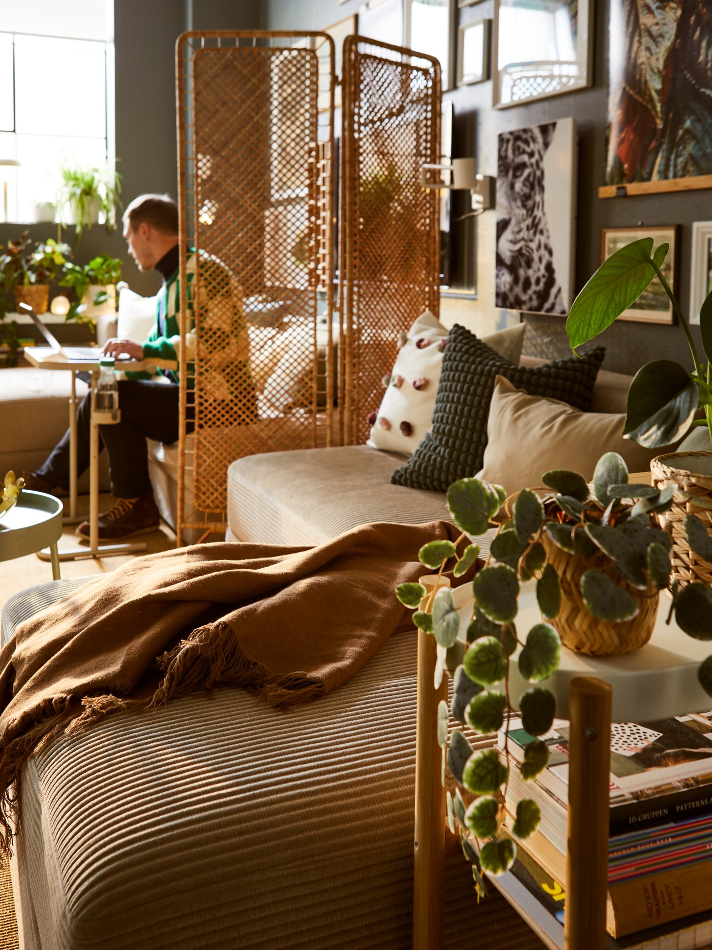 Living room area featuring a JÄTTEBO seat module with storage, a person sitting at a laptop stand, and a room divider.