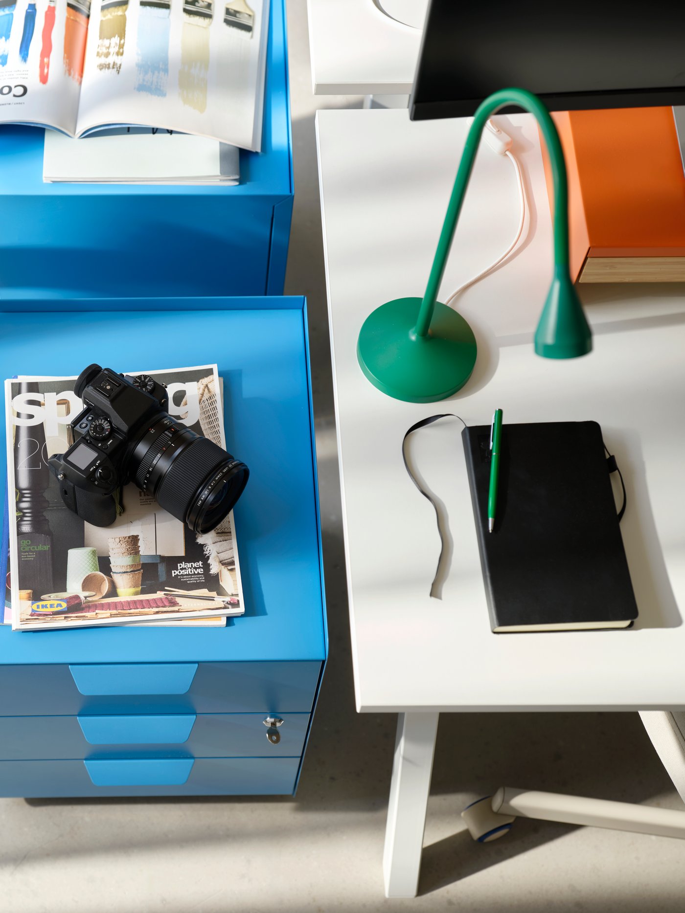 Aerial shot with bright blue storage cabinet on one side and corner of white desk with green angle poise lamp on the other.