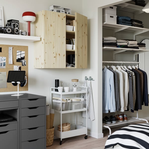 Un armario de pino IVAR fijado a la pared con un carrito de NISSAFORS blanco debajo lleno de cestas de malla de acero.