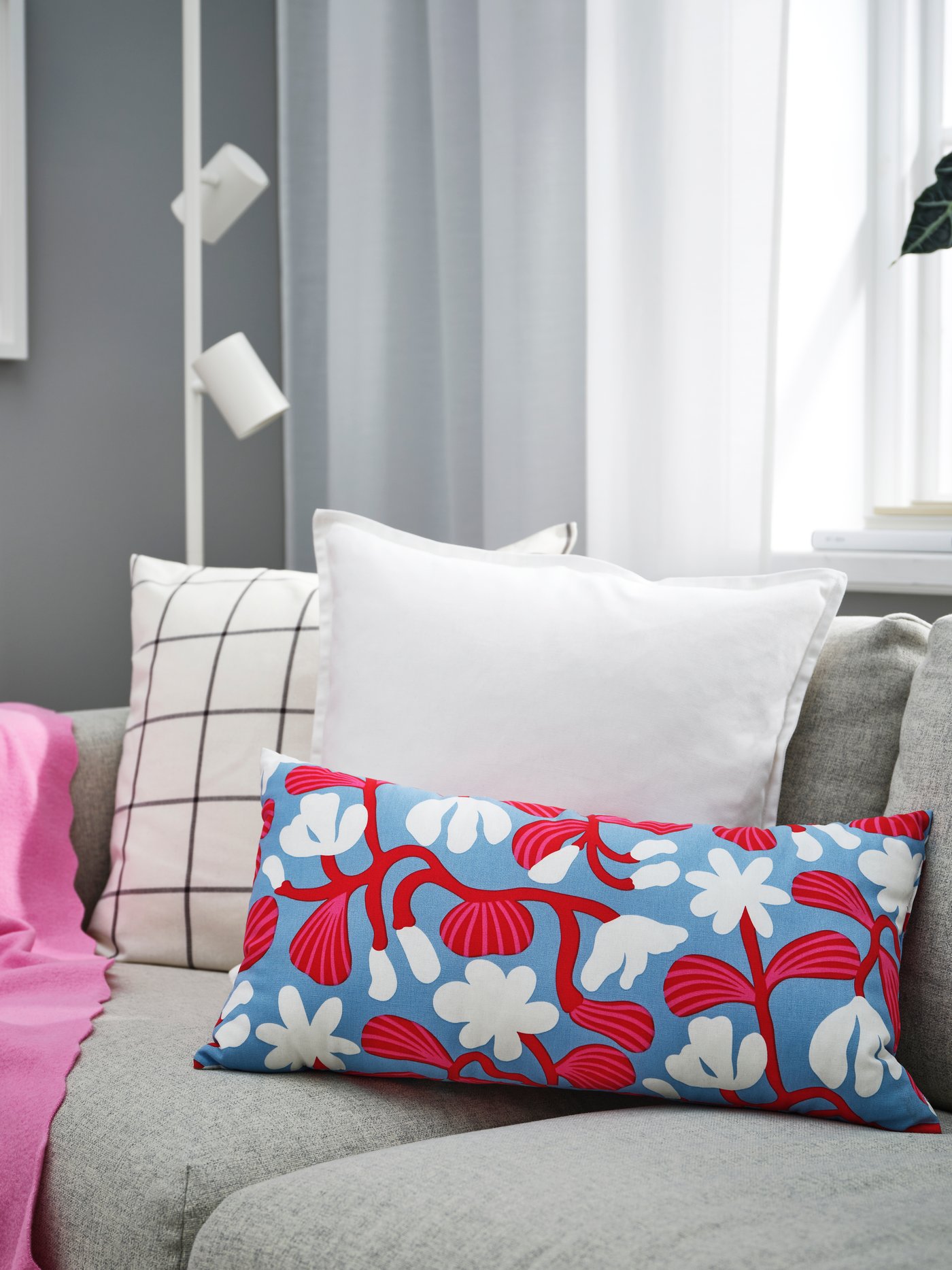 Un divano grigio con vari cuscini fantasia e tinta unita e un plaid rosa.