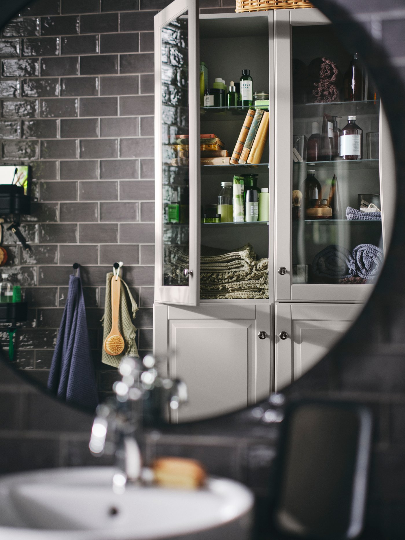 Two light grey GODMORGON high cabinets holding VALLASÅN bath towels and washclothes reflected in a black LINDBYN mirror.
