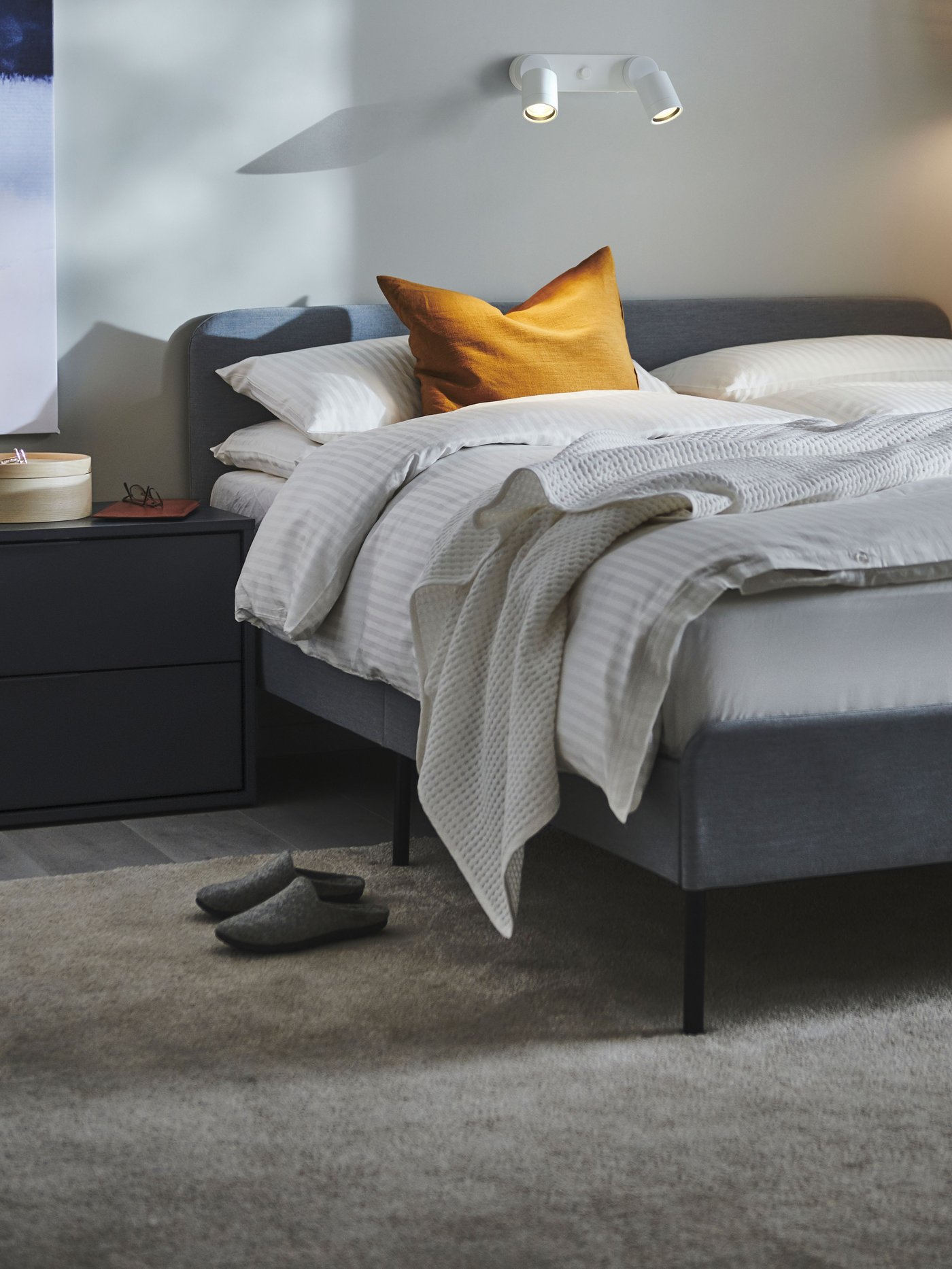 Una cama SLATTUM gris con ropa de cama y mantas encima.